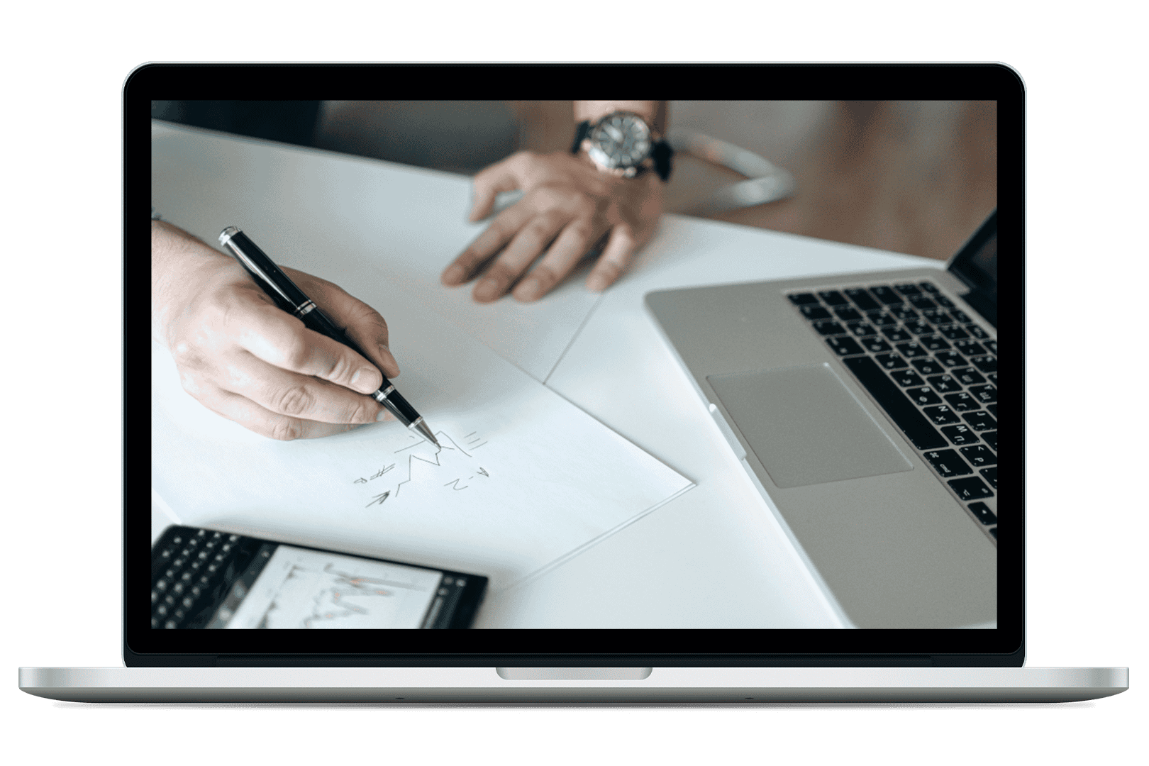 Image of laptop computer with a screen displaying a hand sketching a financial chart on paper beside a laptop and smartphone showing market data.